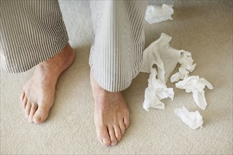 Man's feet surrounded by crumpled tissues. Photo. momentimages