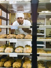 Baker standing behind trays of baked goods. Photo. Erik Isakson