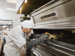 Chef putting bread in oven.