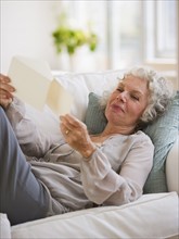 Woman reading mail while relaxing on couch. Photo : Daniel Grill