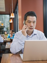 Man talking on phone and working on laptop in restaurant. Photo. Erik Isakson