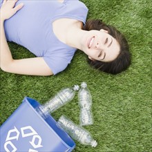 Woman lying on grass beside recycling bin. Photo. Jamie Grill