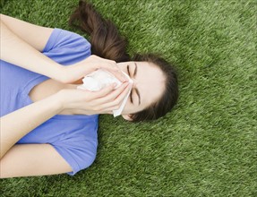 Woman blowing her nose while lying on grass. Photo : Jamie Grill