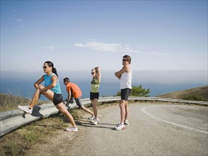Runners stretching on the side of the road.