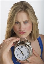 Upset blond woman holding an alarm clock.