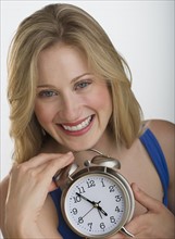 Happy blond woman holding an alarm clock.