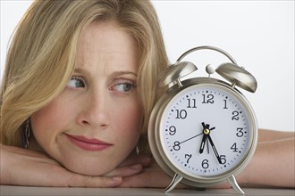 Worried blond woman looking at alarm clock.