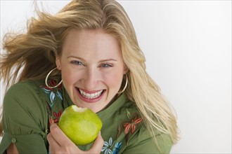 Happy blond woman eating an apple.
