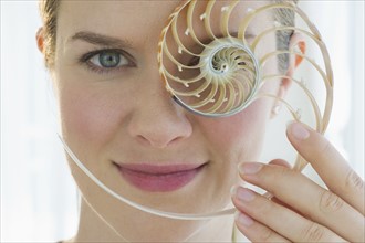 Woman holding a nautilus shell in front of her eye.