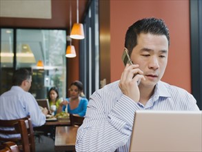 Man talking on phone and working on laptop in restaurant.