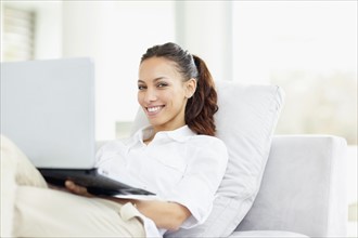 Woman relaxing on couch with laptop. Photo. momentimages