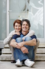 Couple sitting on steps in front of their home. Photo. momentimages