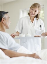 Nurse giving tray of food to patient. Photo. momentimages