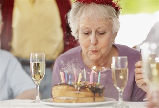 Senior woman blowing out the candles on a birthday cake. Photo. momentimages