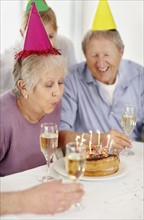 Senior woman blowing out the candles on a birthday cake. Photo. momentimages
