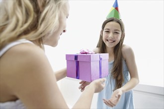 Young girl giving a birthday present to her friend. Photo. momentimages