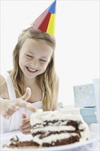 Young girl putting her finger in icing on birthday cake. Photo : momentimages