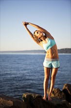 Athletic woman stretching by the ocean. Photo. Take A Pix Media