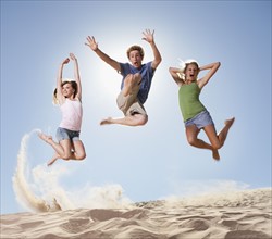 Three people jumping in the sand. Photo : Mike Kemp