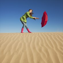 Woman holding red umbrella in the desert. Photo : Mike Kemp