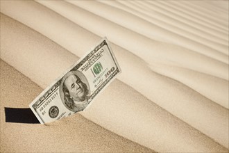 100 dollar bill in sand. Photo : Mike Kemp