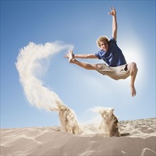 Energetic man jumping in the sand. Photo. Mike Kemp