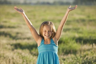 Young girl standing in field with her arms raised. Photo. Mike Kemp