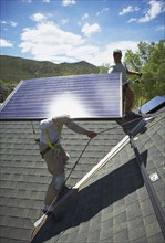 Construction workers installing solar panels on roof. Photo. Shawn O'Connor