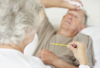 Senior woman caring for man with a fever. Photo. momentimages