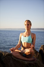 Athletic woman meditating by the ocean. Photo : Take A Pix Media