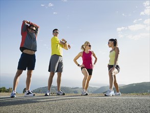Runners stretching on the side of the road.