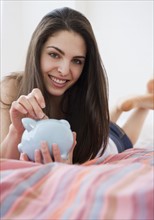 Woman putting coins in piggy bank. Photo. Jamie Grill