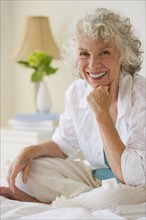 Portrait of a gray haired woman sitting on bed. Photo : Daniel Grill