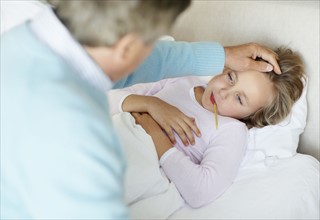 Grandfather tending granddaughter (10-11) lying in bed with thermometer in mouth. Photo :