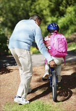 Rear view of grandfather helping granddaughter (10-11) riding bike. Photo : Momentimages