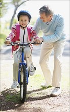 Grandfather helping granddaughter (10-11) riding bike. Photo : Momentimages