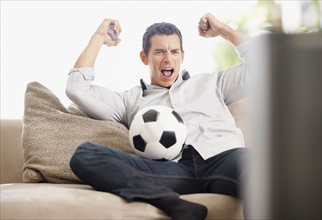 Mid adult man watching football match on television. Photo : Momentimages