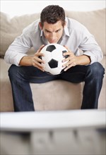 Mid adult man watching football match on television. Photo : Momentimages