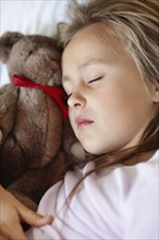 Sad girl (10-11) sleeping in bed with teddybear. Photo : Momentimages