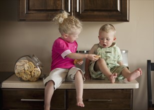 Baby boy and girl (1-3) sharing cookies on kitchen worktop. Photo : Mike Kemp