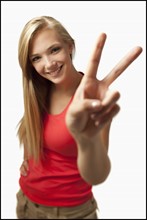 Young woman on white background showing peace sign. Photo : Mike Kemp