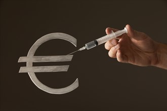 Hand holding syringe on "Euro" sign. Photo : Mike Kemp