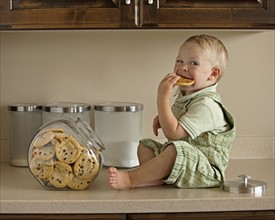 Baby boy (12-17 months) eating cookies on kitchen worktop. Photo : Mike Kemp
