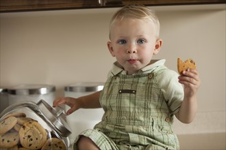 Portrait of baby boy (12-17 months) holding cookie in kitchen. Photo : Mike Kemp