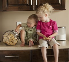 Baby boy and girl (1-3) sharing cookies on kitchen worktop. Photo : Mike Kemp