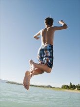 Boy (12-13) jumping into lake.