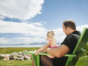 Father and daughter sitting (2-3) on chair and looking at view.