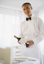 Smiling waiter holding champagne bottle and looking at camera. Photo : Jamie Grill