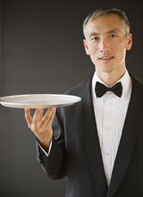 Waiter wearing bow tie and holding tray, studio shot. Photo : Jamie Grill