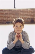 Cute young boy sitting cross legged. Photo : Fisher Litwin